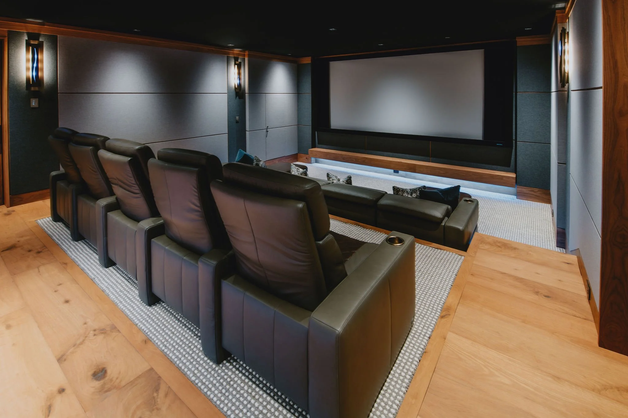 Experience the cinema at home. This modern, dedicated home theater boasts comfortable, reclining black leather seats, premium acoustic paneling, and a large projection screen for the ultimate movie night. View luxury A/V and home automation designs.